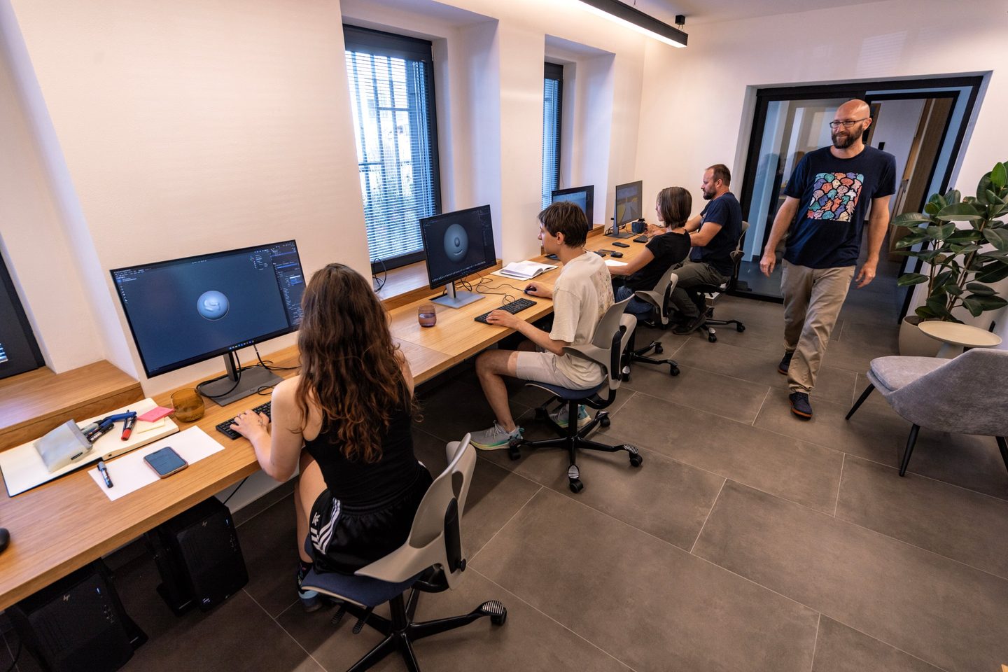 Pět lidí pracuje u monitorů, jeden prochází kolem